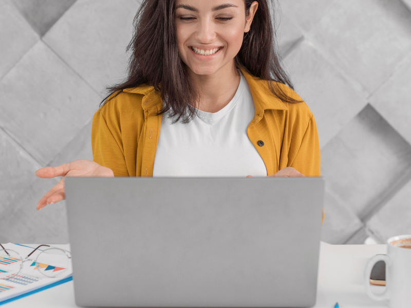 A imagem mostra uma mulher sorrindo enquanto interage com um laptop, possivelmente durante uma chamada de vídeo ou reunião virtual.