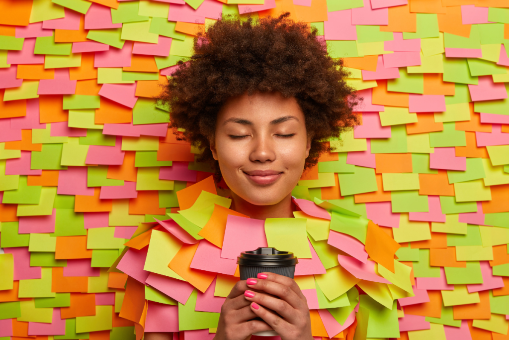 a foto é um retrato alegre e de cores vivas que mostra uma mulher relaxada, segurando um copo de café, emoldurada por uma colagem de notas adesivas coloridas