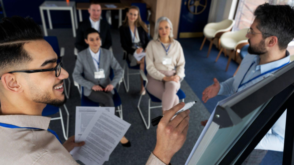 A imagem mostra uma reunião ou sessão de treinamento corporativo em um ambiente de escritório moderno.